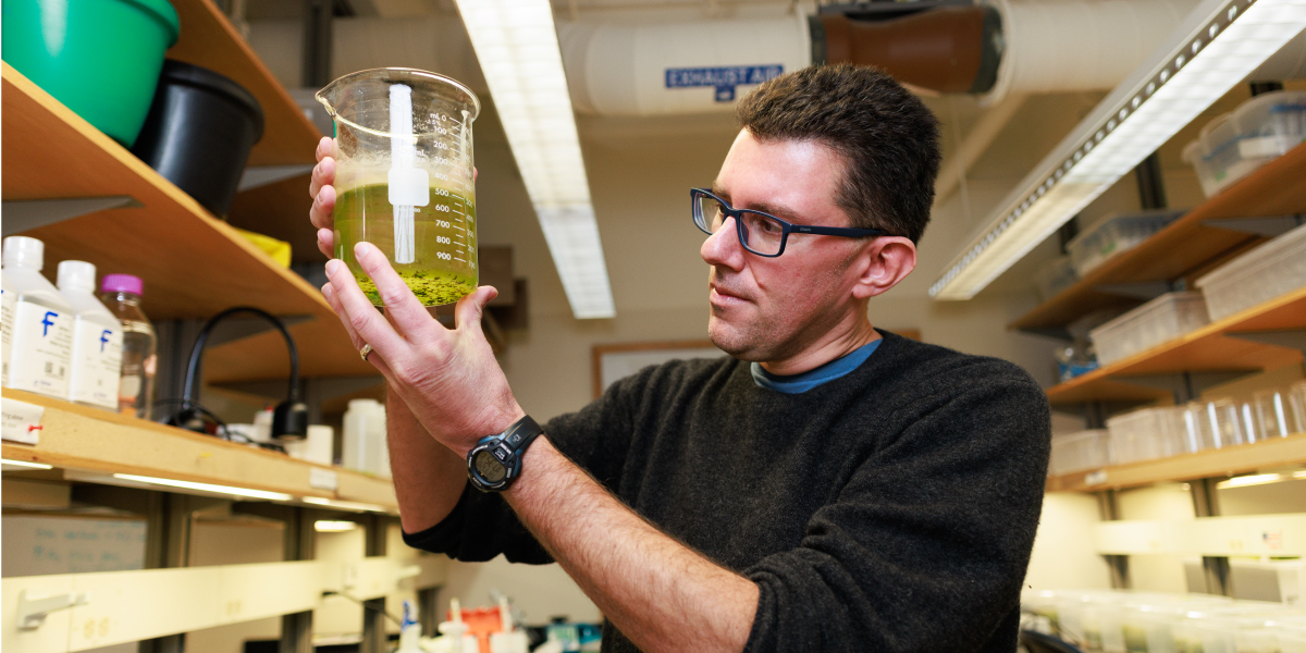 Mark Christie in his lab holding a beaker full of liquid
